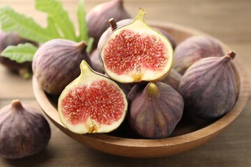 Fresh ripe figs and green leaf in bowl on wooden table, closeup