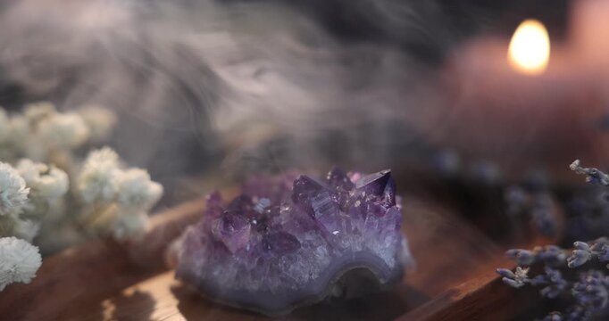 Beautiful amethyst gemstone, flowers and burning candles on table in smoke, closeup