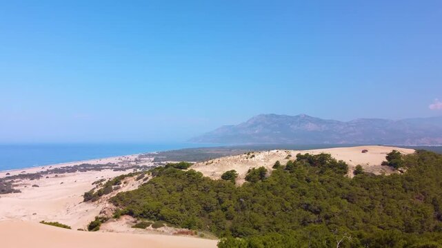 aerial drone footage capturing the vast, golden Patara Sand Dunes meeting the turquoise Mediterranean Sea in Turkey. This panoramic view showcases the unique desert-like landscape of the dunes, the ex