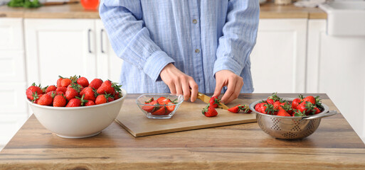 Woman cutting tasty strawberries on table in kitchen