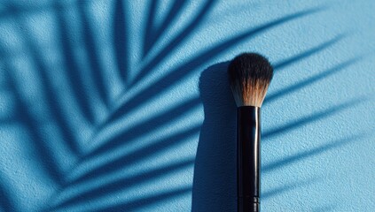Makeup brush casts shadow of palm frond on vibrant blue background