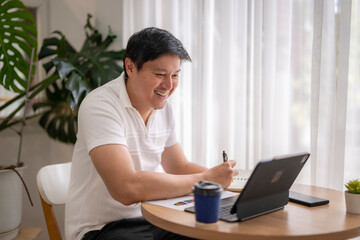 Asian freelancer smiling and working from home using tablet and taking notes