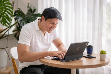 Asian freelancer working from home using tablet and keyboard at coffee table