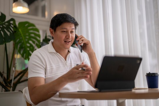 Asian freelancer talking on phone and looking at tablet in cafe