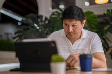 Focused asian freelancer working remotely on tablet in coworking space