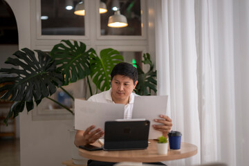 Asian entrepreneur reviewing documents and using tablet in cozy cafe