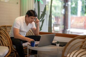 Asian freelancer working remotely from cafe using laptop and thinking hard
