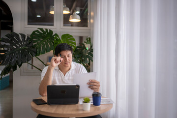 Asian freelancer working from coffee shop reading documents and using tablet
