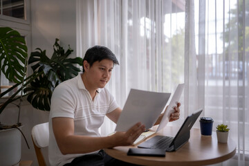 Asian freelancer reading documents and working remotely from home office