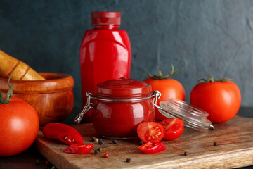 Jar and bottle with tasty ketchup on blue grunge background