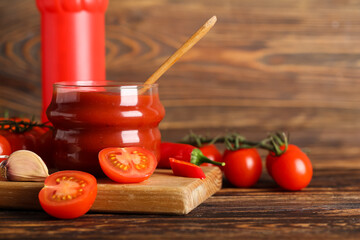Jar with ketchup and ingredients on wooden background