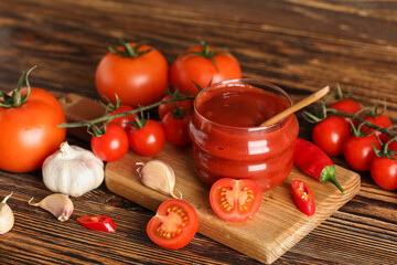 Jar with ketchup and ingredients on wooden background