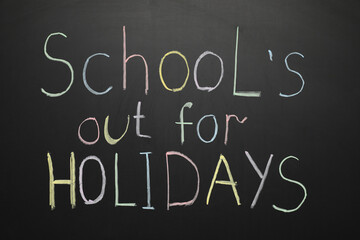 Obraz premium Text SCHOOL'S OUT FOR HOLIDAYS on black chalkboard as background, closeup