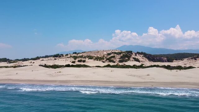 Drone footage captures the stunning aerial perspective of Patara Beach and its expansive sand dunes, a natural wonder located near the ancient city of Patara in Antalya, Turkey. The pristine golden sa
