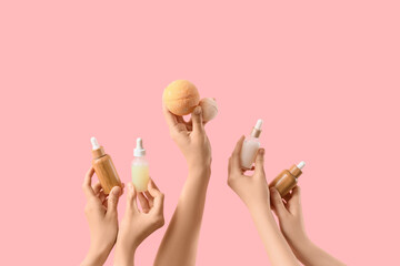 Female hands holding bath bombs and bottles of cosmetic products on pink background