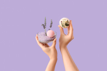 Female hands holding bath bombs and bowl with sea salt on lilac background