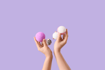 Female hands with different bath bombs on lilac background