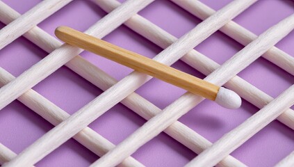A single wooden matchstick rests diagonally on a grid of  white sticks against a lavender background