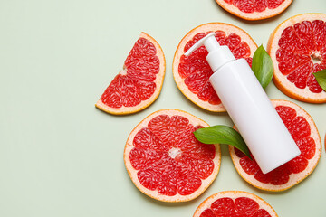 Composition with bottle of cosmetic product and slices of grapefruit on green background, closeup
