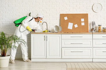 Female pest control specialist disinfecting counter for cockroaches in kitchen