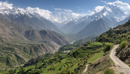 Naklejka premium Panoramic view of a mountain valley with snow-capped peaks, green slopes, and a winding road