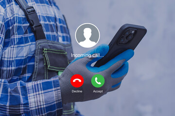 A construction worker wearing protective gloves checks an incoming call on a smartphone. Modern technology use at work.
