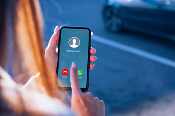 Woman hand with painted nails is seen using a smartphone to either Accept or Decline an incoming call on an urban street on a parking.