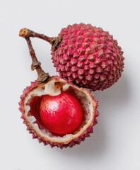 Two red, textured lychee fruits, one split open revealing white flesh and a glistening seed
