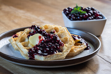 Close-up of golden waffles served with fresh huckleberries, berry jam, and a pat of butter on a...
