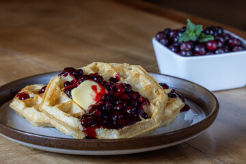 Close-up of golden waffles served with fresh huckleberries, berry jam, and a pat of butter on a rustic plate.