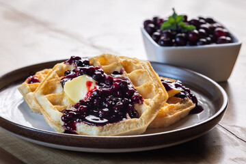 Close-up of golden waffles served with fresh huckleberries, berry jam, and a pat of butter on a rustic plate.