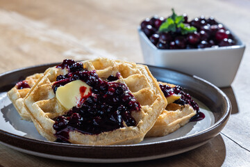 Close-up of golden waffles served with fresh huckleberries, berry jam, and a pat of butter on a rustic plate.