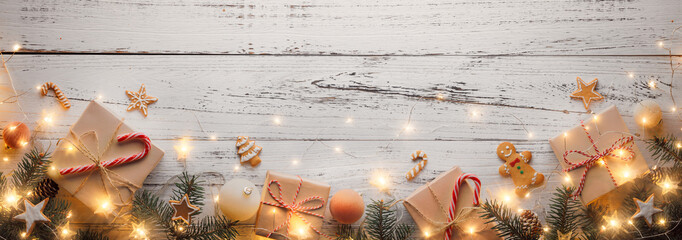 Paper Christmas gift box tied with twine and fir branch with glowing lights on wood background