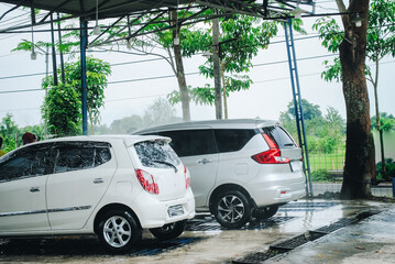 A vehicle is engulfed in soapy foam during a car wash, covering the tires, wheels, hood, and entire exterior of the car. Self-service car wash
