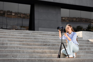 Young happy female photographer with camera and tripod taking photo on stairs in city