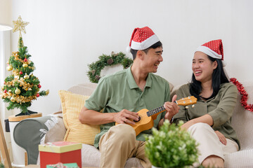 Christmas love, happy couple wears festive hats enjoying winter holiday at home, man plays ukulele for woman, celebrating special christmas time together surrounded by cheerful decorations