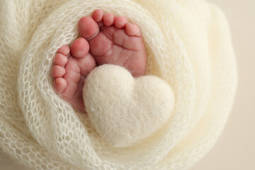 Soft feet of a new born in a white wool blanket. Close up of toes, heels and feet of a newborn. Knitted white heart in the legs of a baby. Macro photography.The tiny foot of a newborn baby