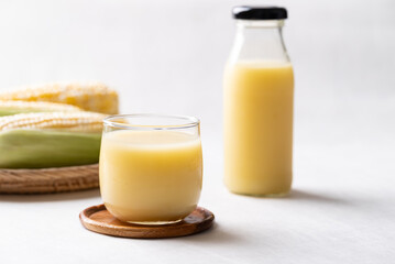 Sweetcorn milk in glass and bottle with fresh sweetcorn on white background, Alternative milk from plant, dairy free