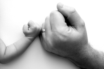 Two hands: man and child. Father and son touching fists. Dad and newborn son boys holding hands together. Little and big fists of father and son. Black and white professional photo. 