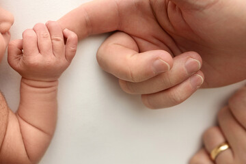 Close-up little hand of child and palm of mother and father. The newborn baby has a firm grip on the parent's finger after birth. A newborn holds on to mom's, dad's finger. 