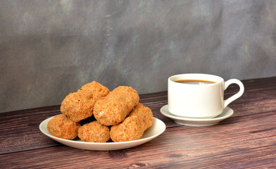 Plate with five fresh eclairs in sprinkles and a cup of hot black coffee on a wooden table.