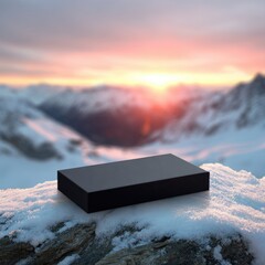 Black product platform on snow-covered mountaintop at sunset