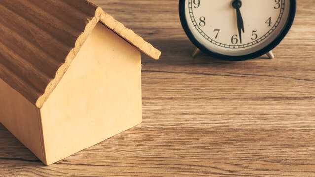 Alarm Clock Next to Wooden House Model Symbolizing Real Estate Deadlines, Time Pressure, and Mortgage Payment Due Dates