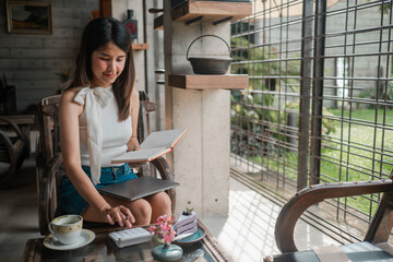 A young woman sits in a modern cafe, reading a book and using a calculator, surrounded by natural light and a cozy atmosphere.
