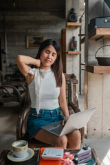 A young woman in casual attire works on her laptop in a stylish cafe with an industrial aesthetic and warm ambiance.