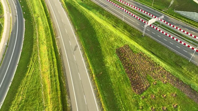 Aerial top-down view of a modern highway (S6 road) cutting through steep green embankments and farmland. Features a single car and traffic barriers