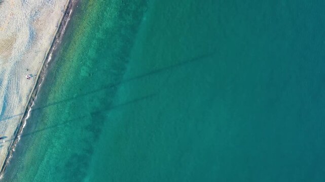 aerial drone shot captures the stunning turquoise waters and pristine sandy beach of Adasi, Turkey. The crystal clear Mediterranean Sea meets the golden shore, showcasing the serene beauty of this coa