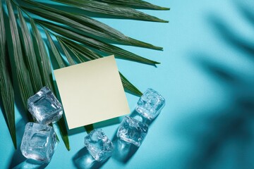 Palm frond, ice cubes, and blank sticky note on turquoise surface with shadows