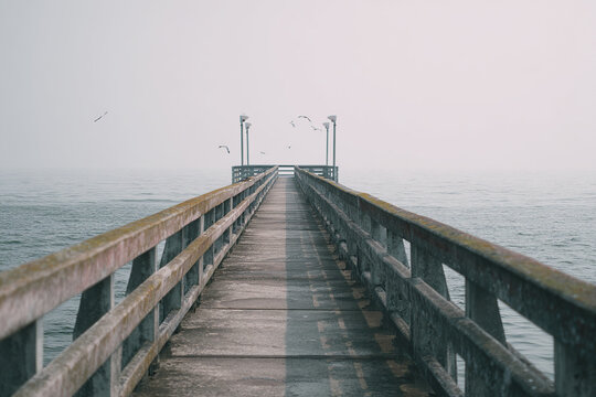 Long wooden pier extending over calm sea under misty sky