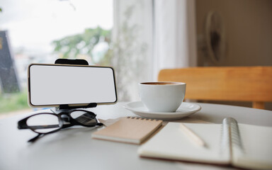 Fototapeta premium smart phone on stand with coffee cup, note book and diary on table